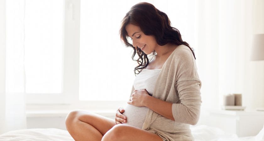 Mulher grávida com as mãos sobre o ventre, simbolizando promessa divina, fé e novos começos espirituais.